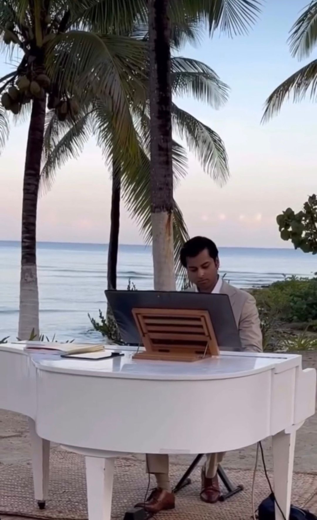 Abishek playing white piano near the ocean, representing voice confidence and personal transformation